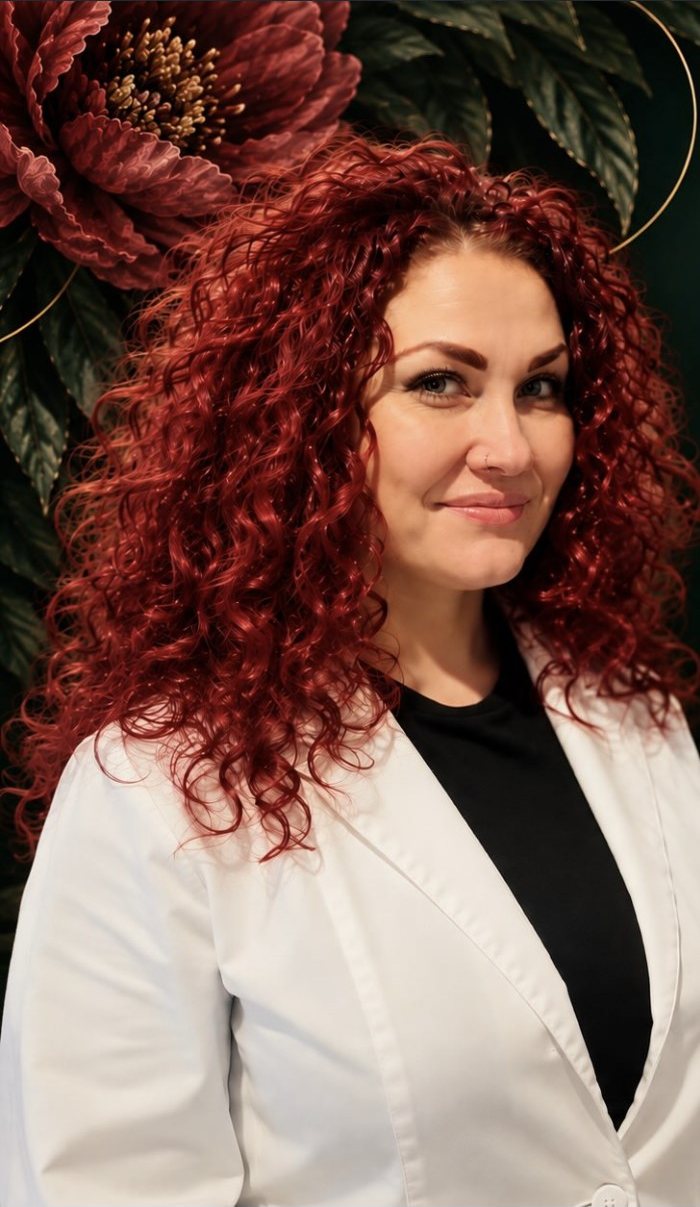 Danielle Anderson, esthetician and owner of Ninth Remedy, in a white blazer in front of the studio's dark botanical backdrop.